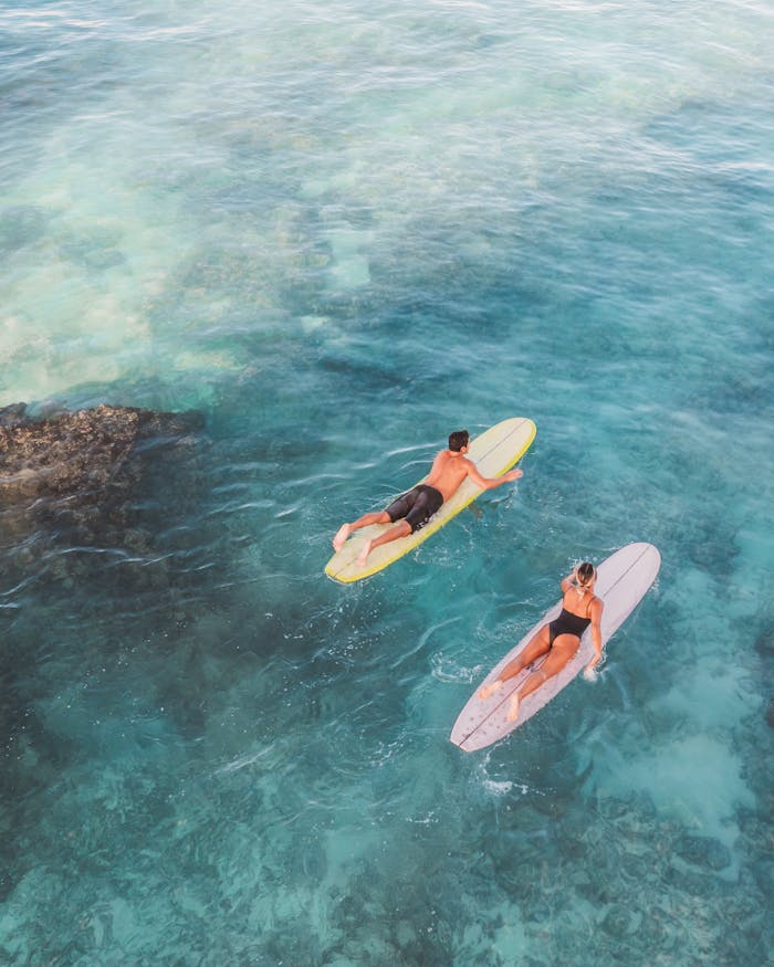 Two surfers paddle through turquoise waters, enjoying a sunny day at the beach.